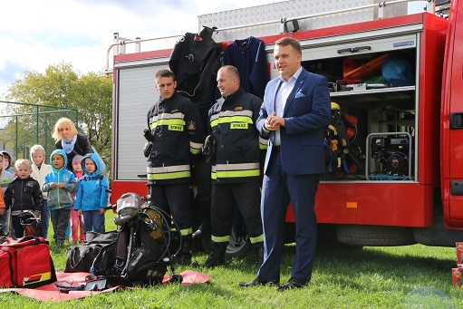 Marek Materek na tle wozu strażackiego podczas pikniku promującego zawód strażaka wśród najmłodszych